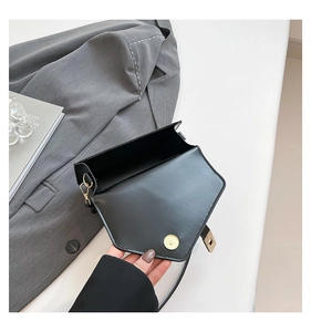 Detail of open black leather crossbody bag with gold magnetic clasp on white desk