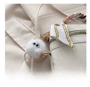 Close-up of fluffy white plush doll charm with big eyes on a white marble bag
