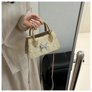 Detail of hand-woven straw bag with floral embroidery and silver metal bow ornament