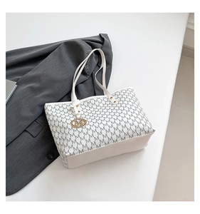 Detail of white tote bag featuring black letter prints and golden M charm pendant