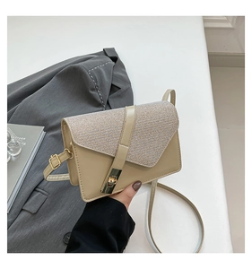 Close-up of beige crossbody bag with textured flap and gold twist lock in lifestyle scene