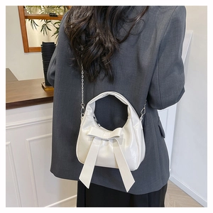 Detail of white glossy leather bucket bag with bow and silver chain strap on a model