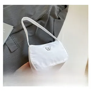 White nylon shoulder underarm bag with silver metal butterfly detail in fashion setting