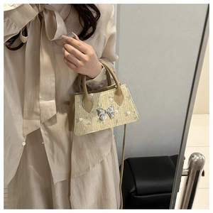 Detail of mini straw bag with blue floral embroidery and silver metal bow on beige texture