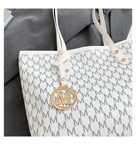 Detail of retro tote bag with monogram print and golden metal M letter pendant accessory