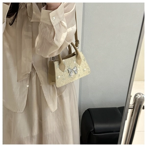 Detail of beige woven crossbody bag with floral embroidery and silver bow hardware
