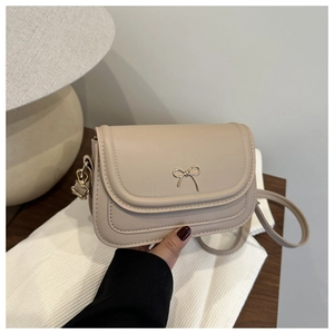 Close-up of beige leather shoulder bag with gold bow clasp on a textured background
