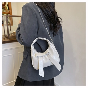 Detailed view of white crescent bag with oversized bow and silver chain strap