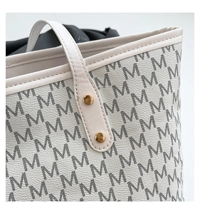 Close-up of white tote bag showing black M-letter print and golden metal rivet details