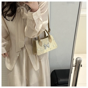 Detailed view of woven beige crossbody bag featuring a silver metal bow buckle accent