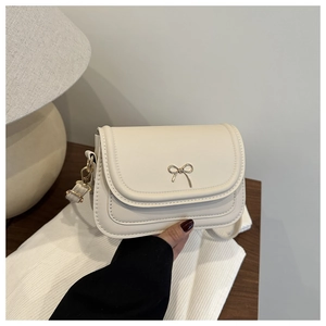 Close-up of cream crossbody bag with golden bow buckle and fine faux leather texture