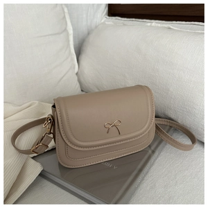 Detail of light beige square crossbody bag featuring a delicate gold bow metal buckle