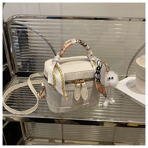 Detail van witte box-handtas met zijden sjaal handvat en pluchen bal-accessoire