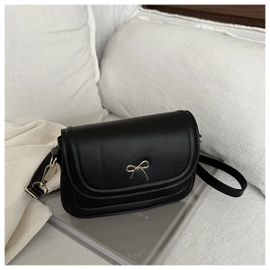 Detail of a matte black leather shoulder bag with a gold bow buckle on a beige textile