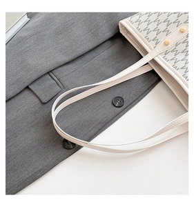 Close-up of beige tote bag with M-letter print and golden rivet hardware details