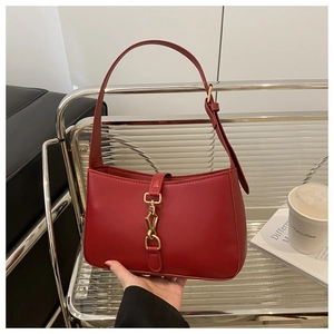 Close-up of red leather underarm bag featuring a vintage golden piston lock buckle