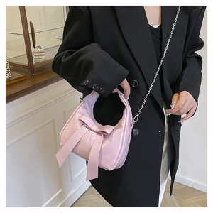 Detail of pink glossy bow handbag with silver chain strap shown in a lifestyle setting