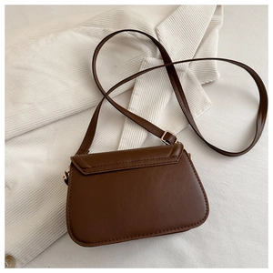 Detail einer braunen Satteltasche aus Leder auf weißem Stoff mit goldener Schnalle