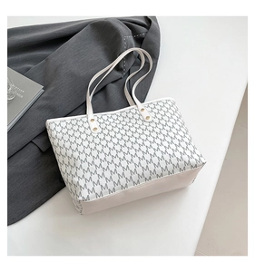 Detail of cream tote bag with grey M-pattern and golden metal rivets on handles