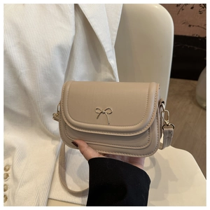 Detail of beige mini square bag featuring a gold bow accent and PU leather texture