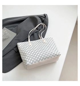Detail of white tote bag with grey monogram print and golden metallic studs