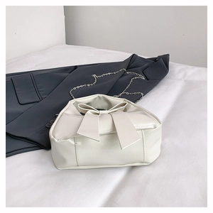 Detailed view of cream bow shoulder bag with silver chain strap on white fabric