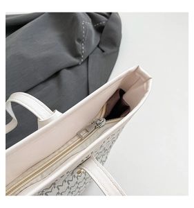 Detail view of the silver zipper closure and M-pattern printed lining on the tote bag
