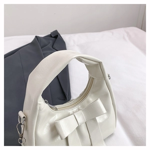 Detail of white glossy hobo bag featuring a large decorative bow and silver zipper
