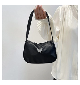 Detail of black nylon underarm bag featuring a white butterfly ornament held by a model