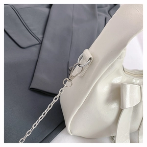 Detail of white glossy dumpling bag with metallic chain and delicate bow decoration