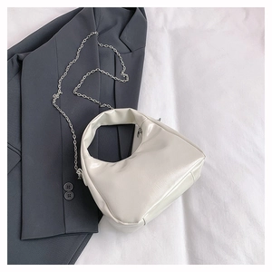 Detail of white glossy dumpling bag with silver metal chain on dark blazer