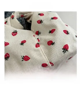 Gros plan sur tissu en velours côtelé blanc avec imprimés fraises rouges et texture fine