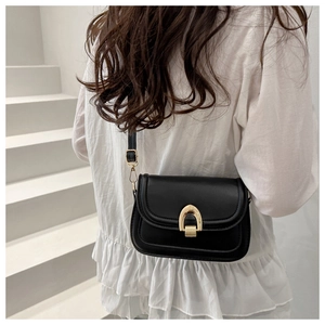 Detail of a chic black saddle bag featuring a gold horseshoe clasp and sleek glossy finish
