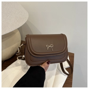 Detailed shot of brown leather saddle bag featuring a gold metal bow buckle and fine strap