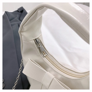 Detail of cream hobo bag featuring a large decorative bow and silver chain strap