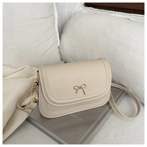Detail of elegant beige square crossbody bag with golden bow hardware clasp and leather strap