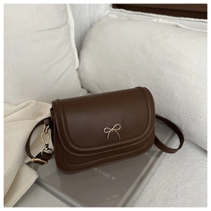 Detail of dark brown square crossbody bag with gold bow clasp on a lifestyle background