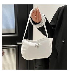 Close-up of white minimalist shoulder bag featuring a silver metal butterfly buckle detail