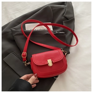 Détail du sac rouge en cuir grainé avec fermoir doré posé sur un blazer gris chic