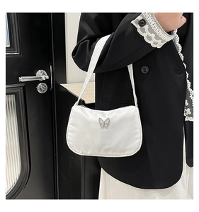 Detail of white satin shoulder bag featuring a metallic butterfly ornament and silky texture