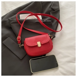 Close-up of red lychee textured saddle bag with gold metal buckle and smartphone for scale
