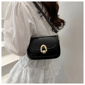 Detail of a minimalist black crossbody bag featuring a gold horseshoe metal buckle