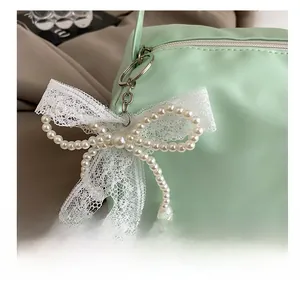 Detail of white pearl beaded bow charm with lace on a mint green leather handbag