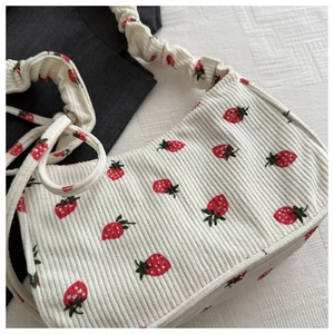Detail of white corduroy shoulder bag featuring red strawberry prints and ruched strap