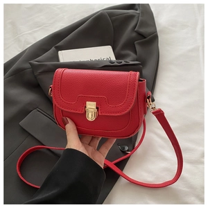 Detail of red saddle bag with lychee texture and gold clasp on a grey suit blazer
