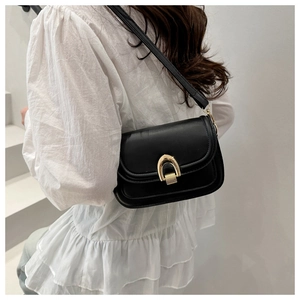 Detail of minimalist black crossbody bag with gold U-shaped metal clasp on white background