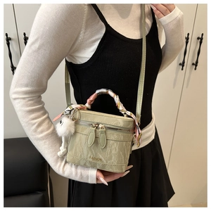 Close-up of light green mini bucket bag with scarf-wrapped handle and plush charm