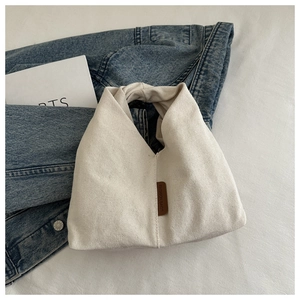 Détail d'un sac à main en toile crème avec étiquette en cuir marron et poignée intégrée