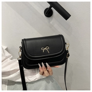 Detail shot of a black mini square bag with a delicate gold bow buckle and shoulder strap