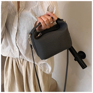 Detail of dark grey woven texture crossbody bag with gold-tone hardware on model